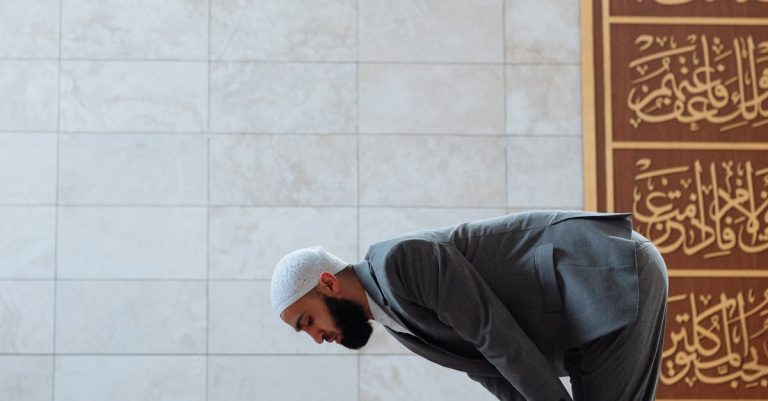 Adult man in prayer inside a mosque, featuring Arabic calligraphy, symbolizing faith and devotion.